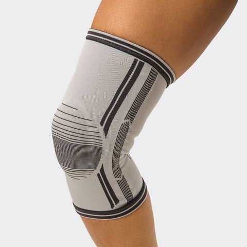 Grey Thermoskin Dynamic Compression Knee Stabiliser worn on a knee, with knitted support panels either side